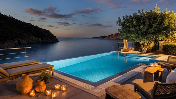 A poolside area with lounge chairs, candles, and a view of the sea at dusk.