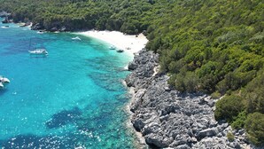A coastal area with clear turquoise waters, rocky shoreline, and boats anchored near the beach.