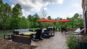An outdoor patio with a sofa, chairs, and tables, surrounded by trees and a stone building. - Hampton Inn Black Mountain (Black Mountain)
