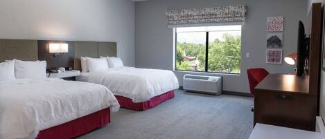 A hotel room with two beds, a desk, a chair, a window with a view, and a wall-mounted TV.