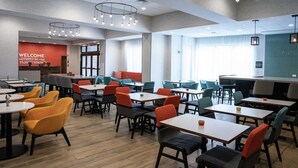 A modern dining area with tables and chairs, a 'WELCOME' sign, and a view of the outside. - Hampton Inn Black Mountain (Black Mountain)