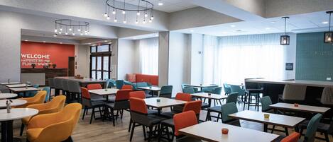 A modern dining area with tables and chairs, a 'WELCOME' sign, and a view of the outside.