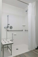 Un baño moderno con ducha, barras de apoyo, un lavabo blanco y cortina de ducha.