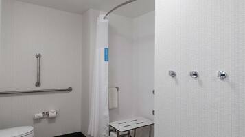 Un baño con inodoro blanco, ducha con puerta curva, barra de apoyo y toallero.