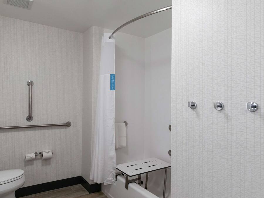 Un baño con inodoro blanco, ducha con puerta curva, barra de apoyo y toallero.