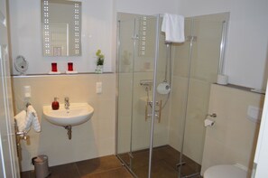 A modern bathroom with a glass-enclosed shower, a sink with a mirror above, and a toilet. - Altstadtpension Hameln (Hamelin)