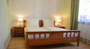 A wooden bed with two nightstands, each with a lamp, in a room with floral wallpaper and wooden flooring. - Altstadtpension Hameln (Hamelin)