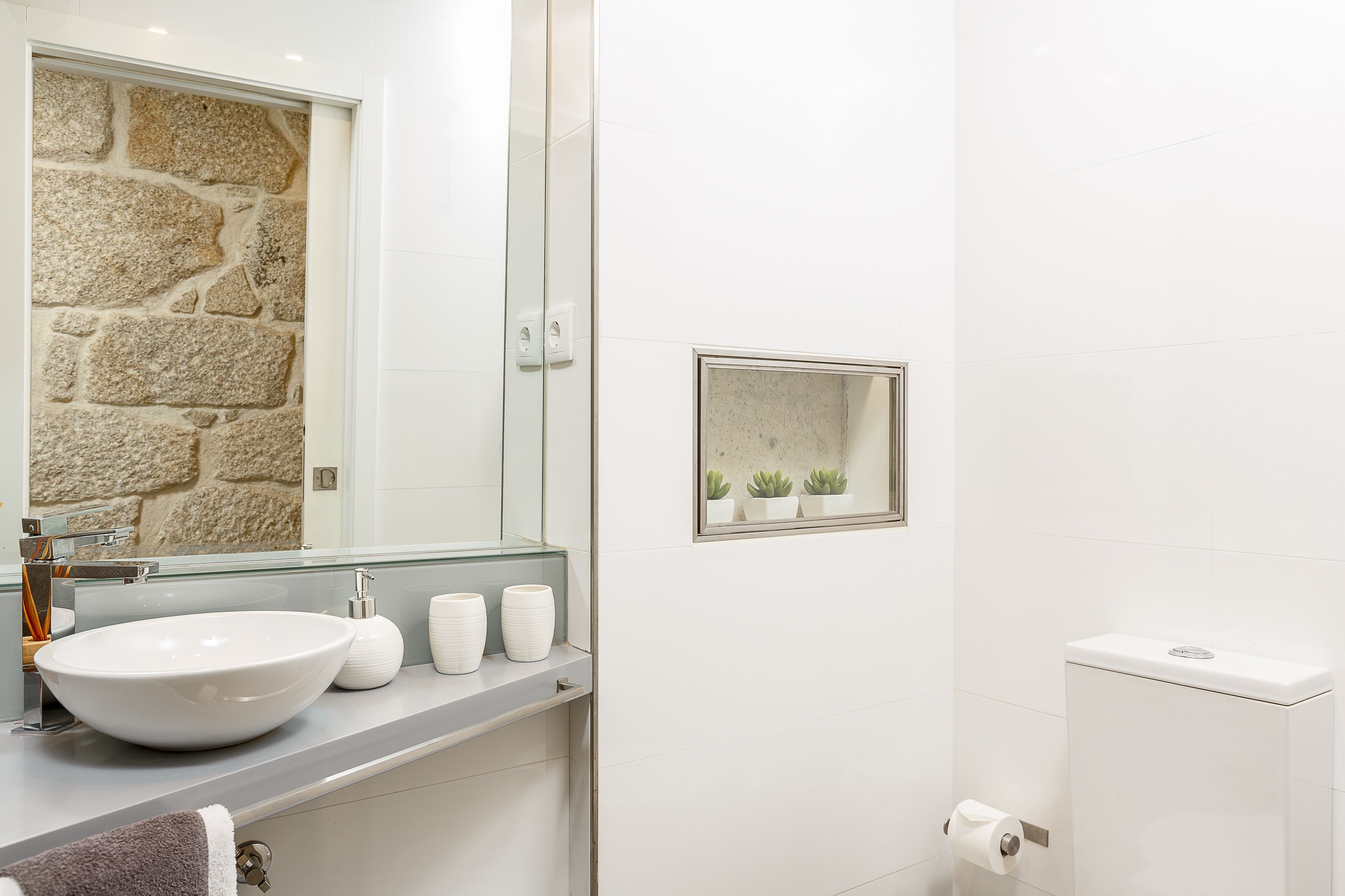 A bathroom with a stone wall, a large mirror, a white sink, and a toilet.