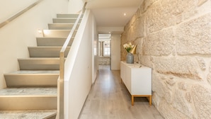 A modern staircase with a stone wall on one side and a white console table with a vase on the other. - YOUROPO - Ribeira Porto (Porto)