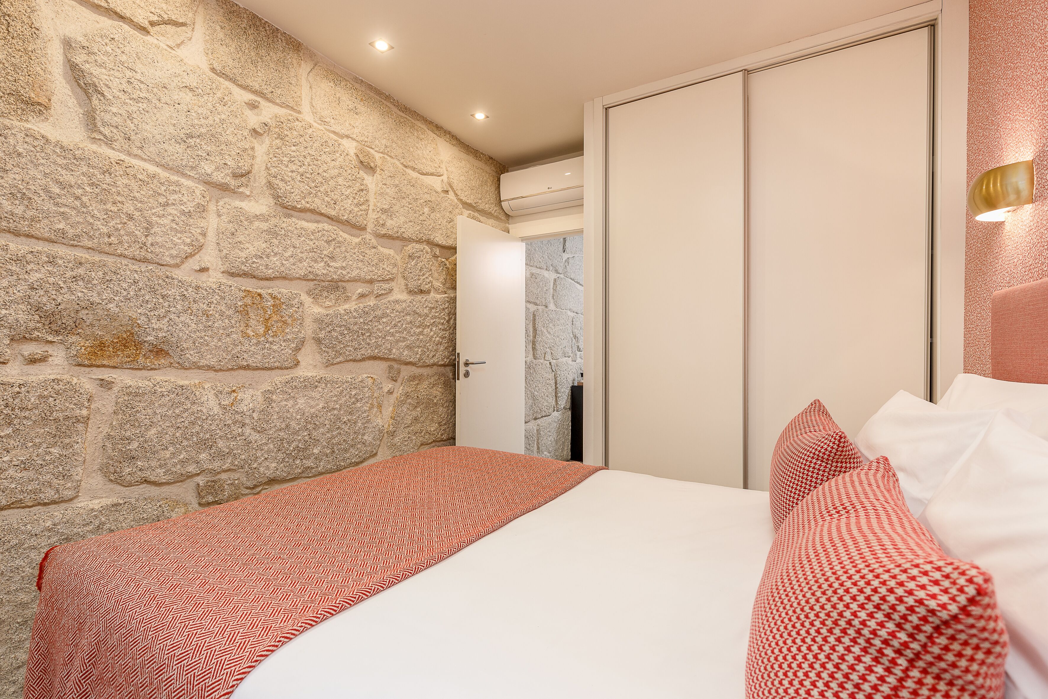 Un dormitorio con pared de piedra, cama con colcha estampada y armario.