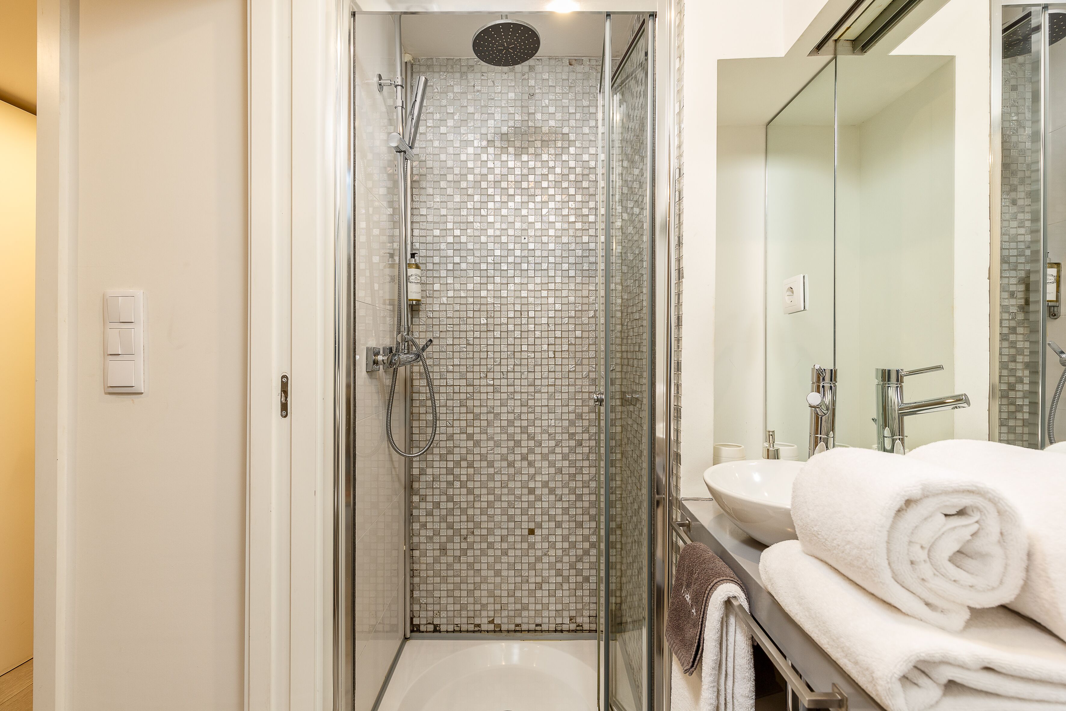 A modern bathroom with a glass-enclosed shower, a white sink, and a large mirror.