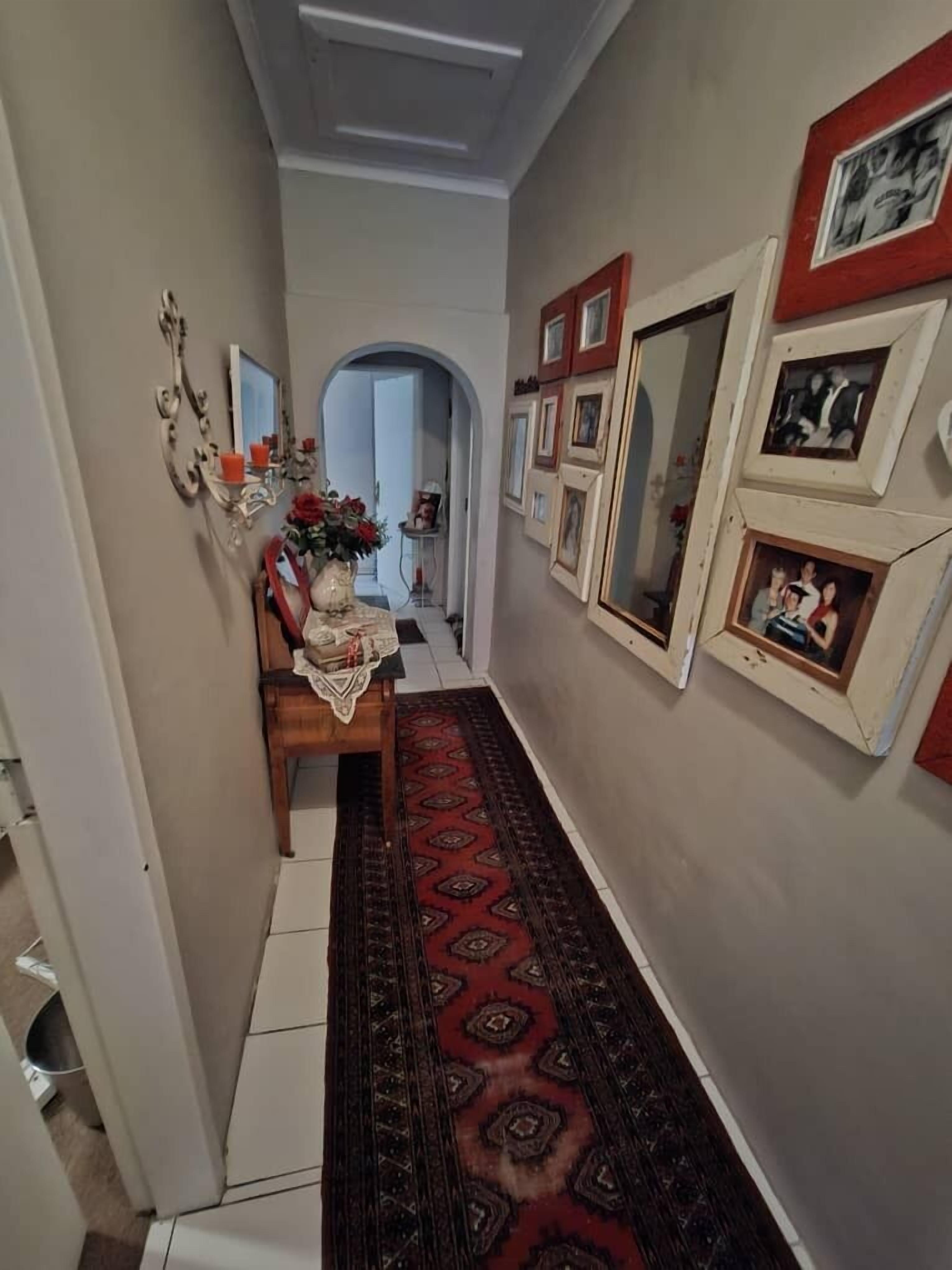 A hallway with a patterned rug, a wooden bench, a mirror, and framed pictures on the walls.