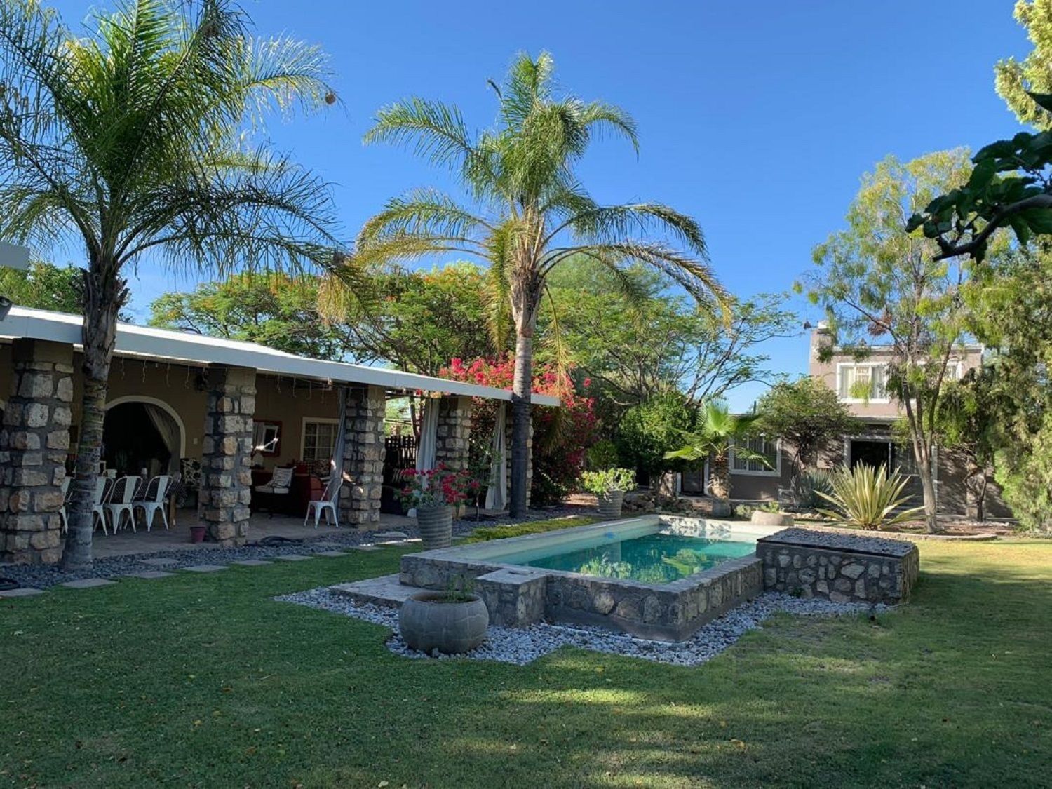 A stone house with a covered patio, a swimming pool, and a well-maintained garden with various plants and trees.
