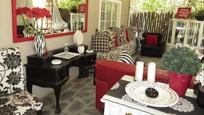 Un salón acogedor con un espejo grande, un sofá estampado y un sillón rojo. Hay una mesita con velas y un jarrón de flores.