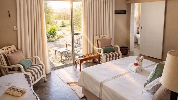 Un dormitorio con cama, dos sillas, una mesita y vistas al jardín.