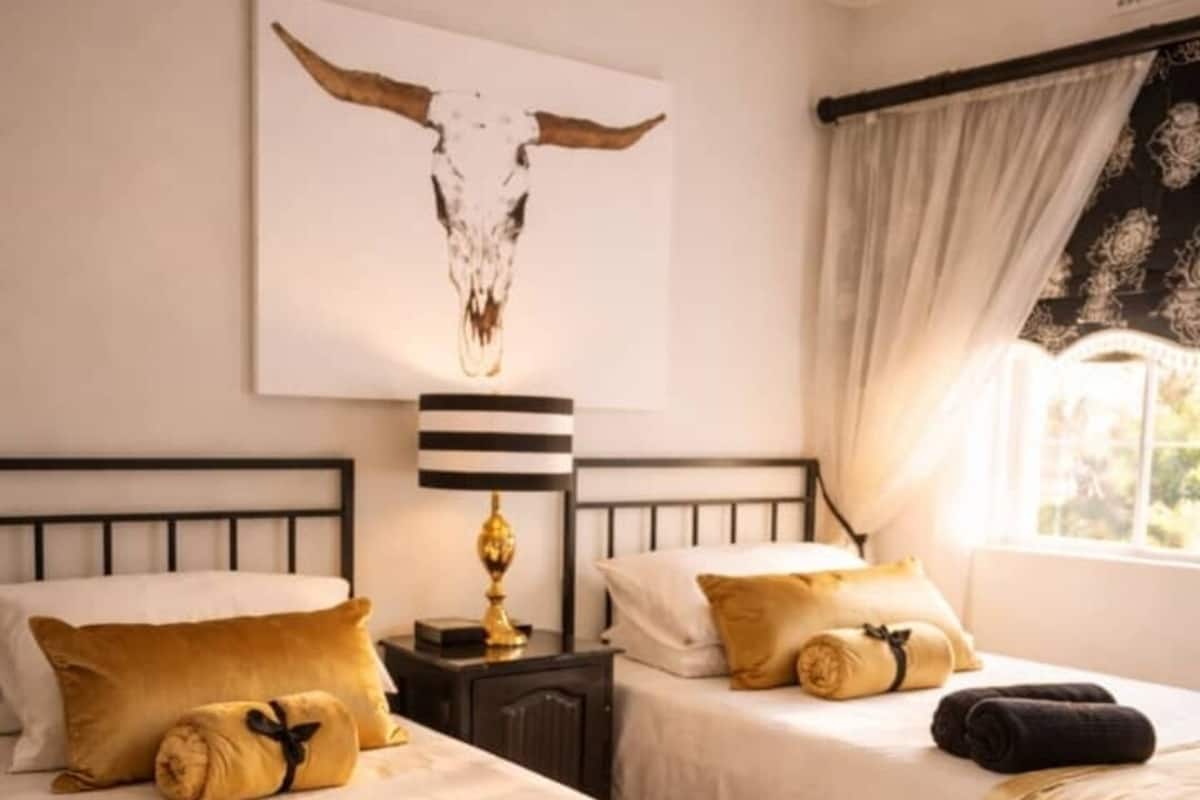 Hotellihuone, jossa on kaksi sänkyä, yöpöytä lampun kanssa, seinälle ripustettu taideteos ja ikkuna, jossa on verhot.