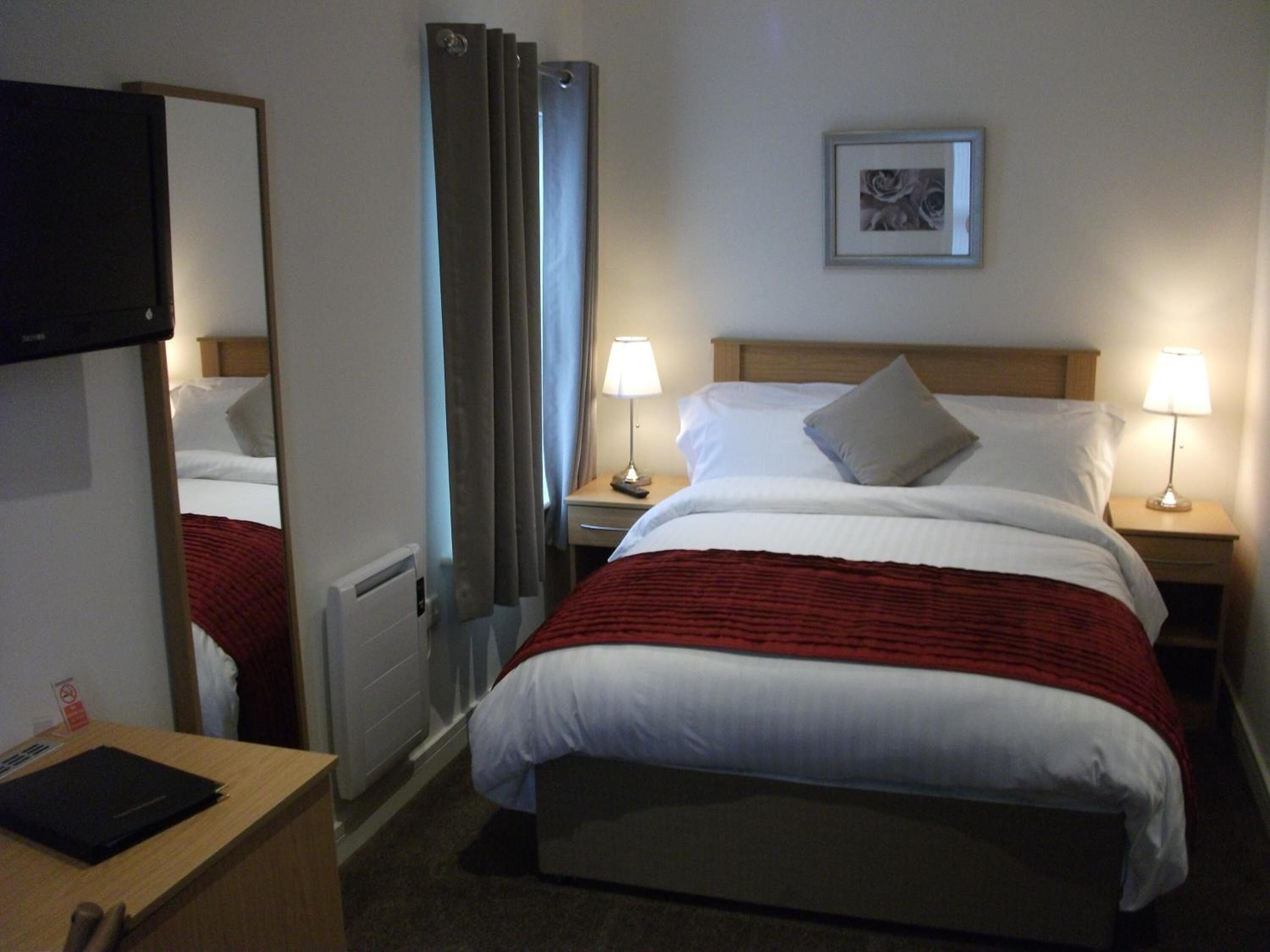 Hotelkamer met een bed, twee bedlampen, een ingelijst schilderij aan de muur, een spiegel en een bureau met een zwart mapje.