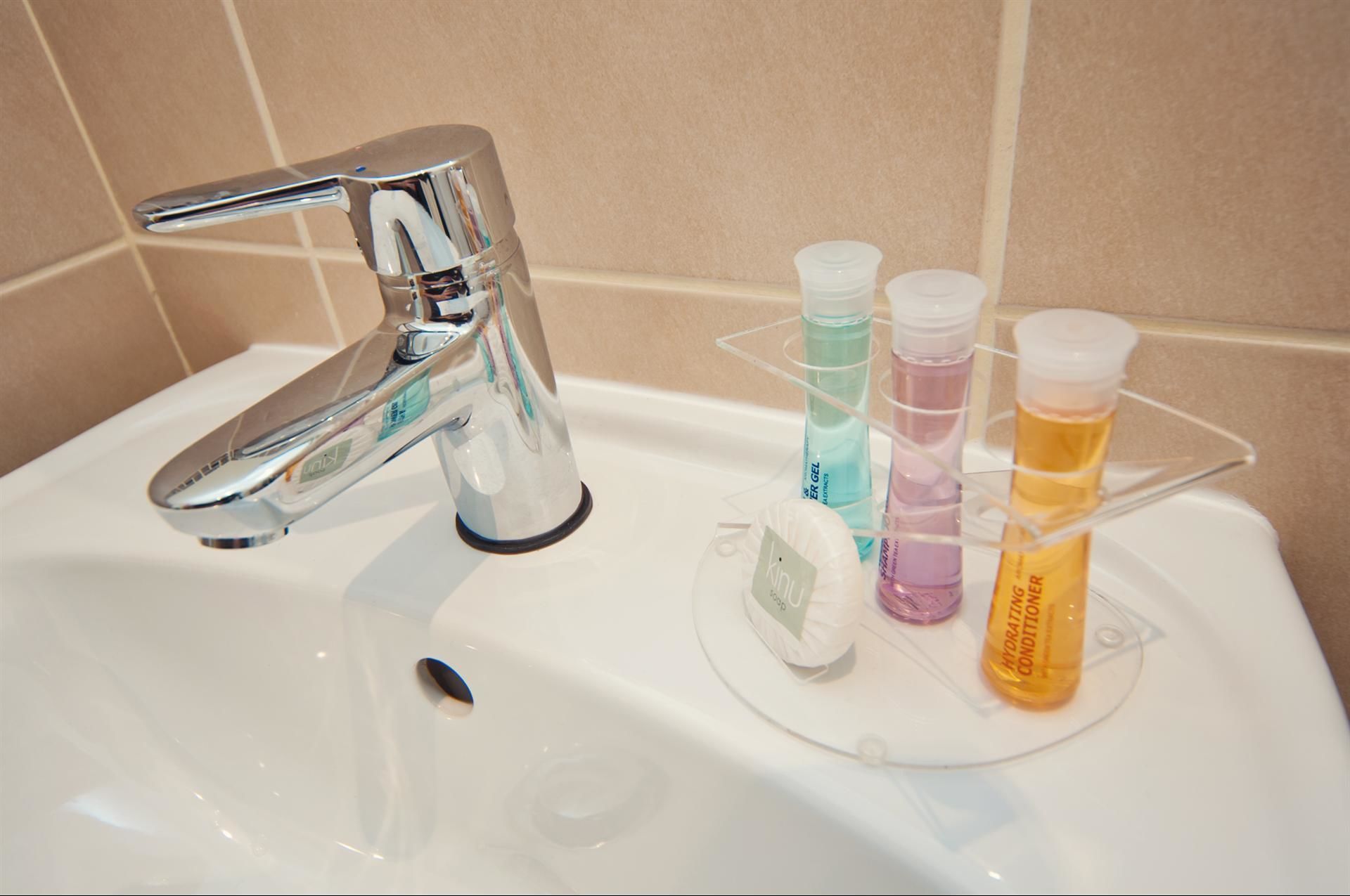 Un lavandino da bagno con un rubinetto cromato, un dispenser di sapone e un portaposate con tre flaconi di sapone liquido.