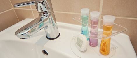A bathroom sink with a chrome faucet, a soap dispenser, and a soap dish holding three bottles of liquid soap.