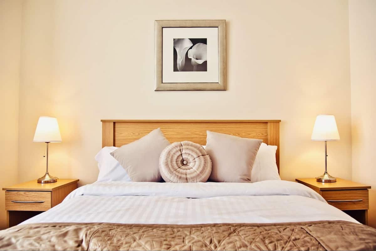 A neatly made bed with a wooden headboard, two bedside tables with lamps, and a framed picture on the wall.