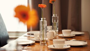 A dining table set with white plates, cups, and a clear vase with a single orange flower. - The Burlington Hotel (Cleethorpes)