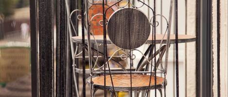 A metal-framed chair with a round cushion on a wooden deck, enclosed by a black metal railing.