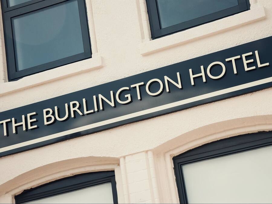 Ein Schild mit der Aufschrift "The Burlington Hotel", gestaltet im klassischen Stil mit Bogenfenstern und einer klaren Fassade.