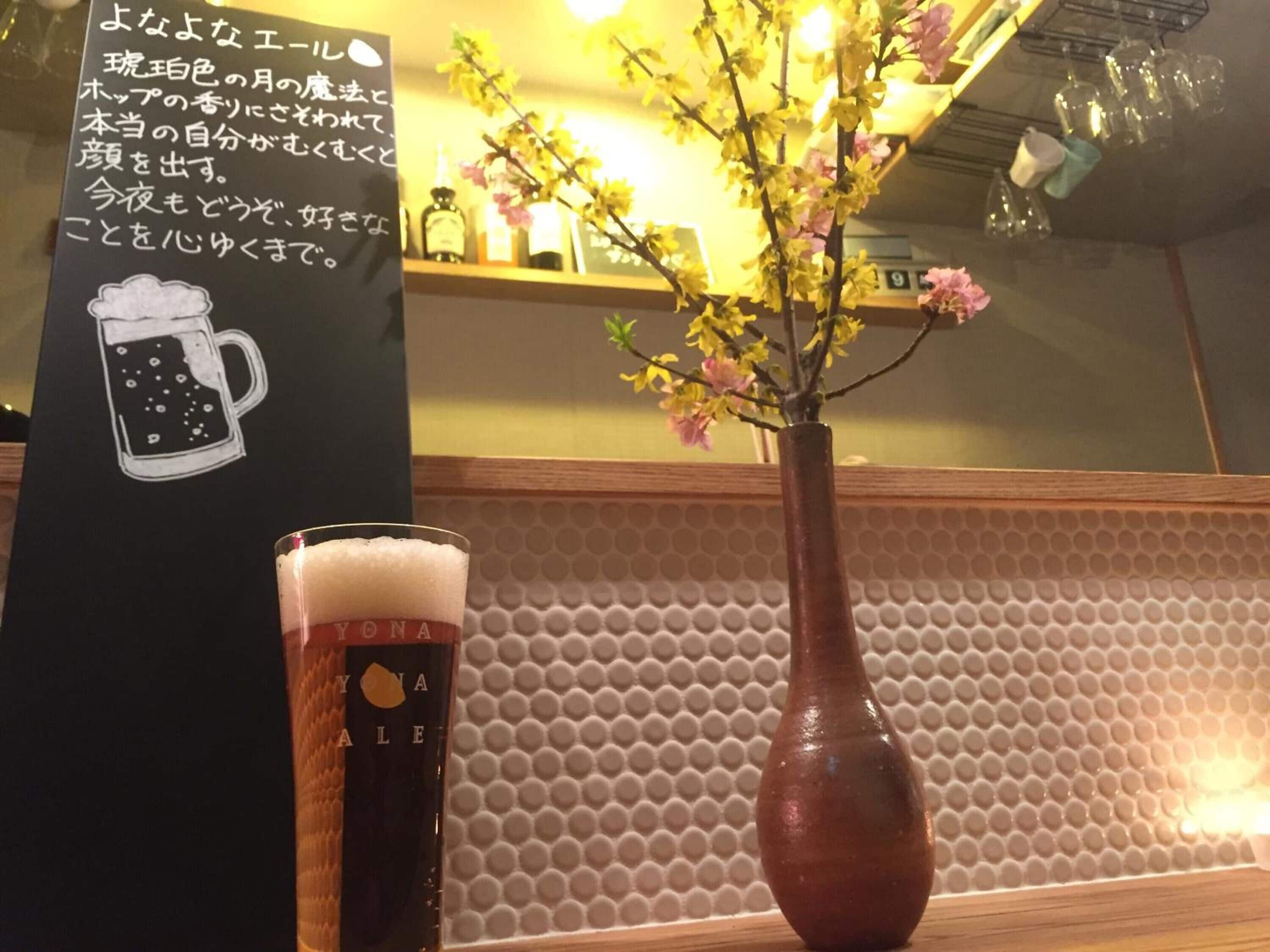 Un verre de bière à côté d’un vase rempli de fleurs, posé sur le comptoir d’un bar.