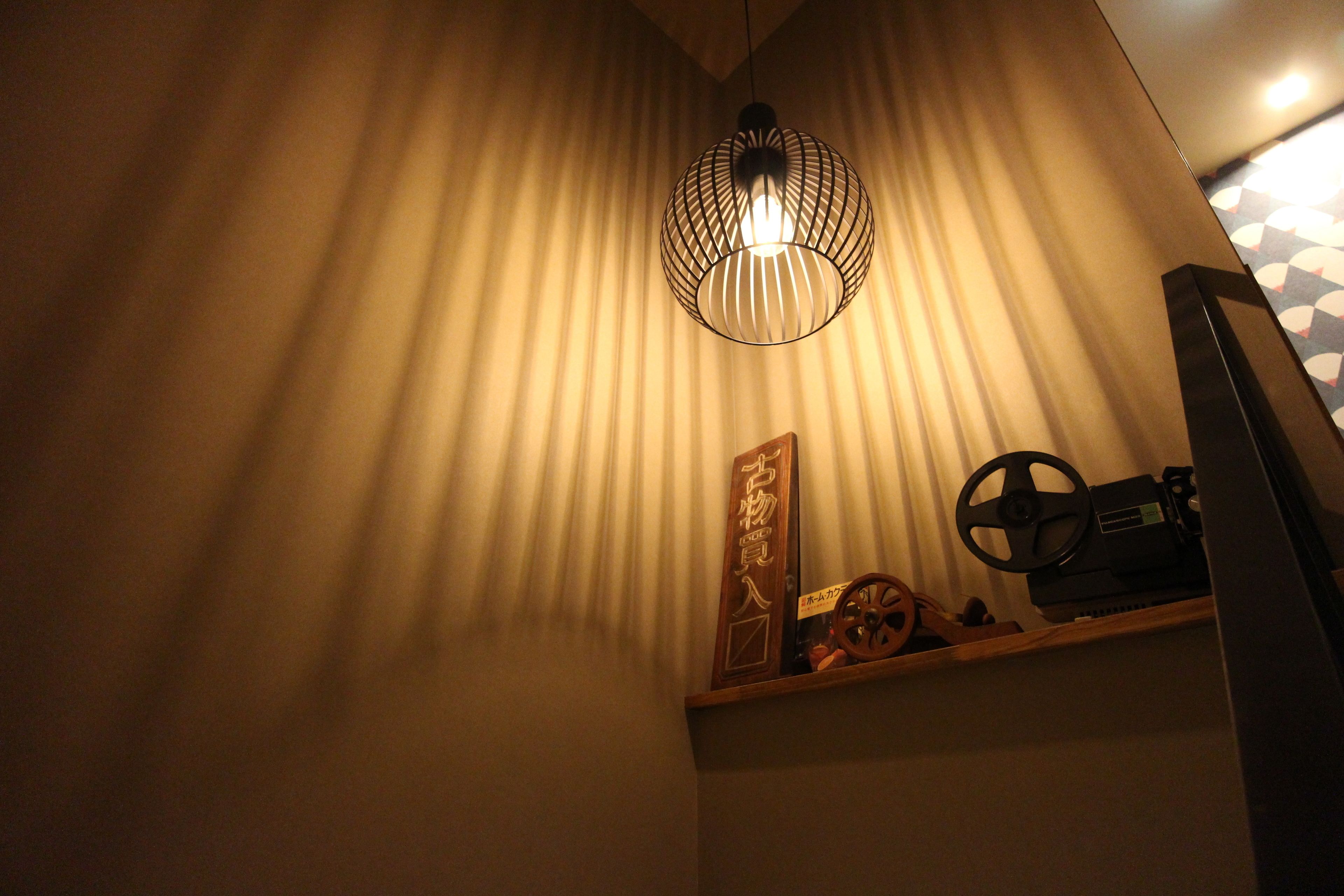 A room with a slatted ceiling light fixture, a wooden shelf with decorative items, and a patterned wall.