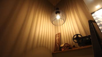 A room with a slatted ceiling light fixture, a wooden shelf with decorative items, and a patterned wall.