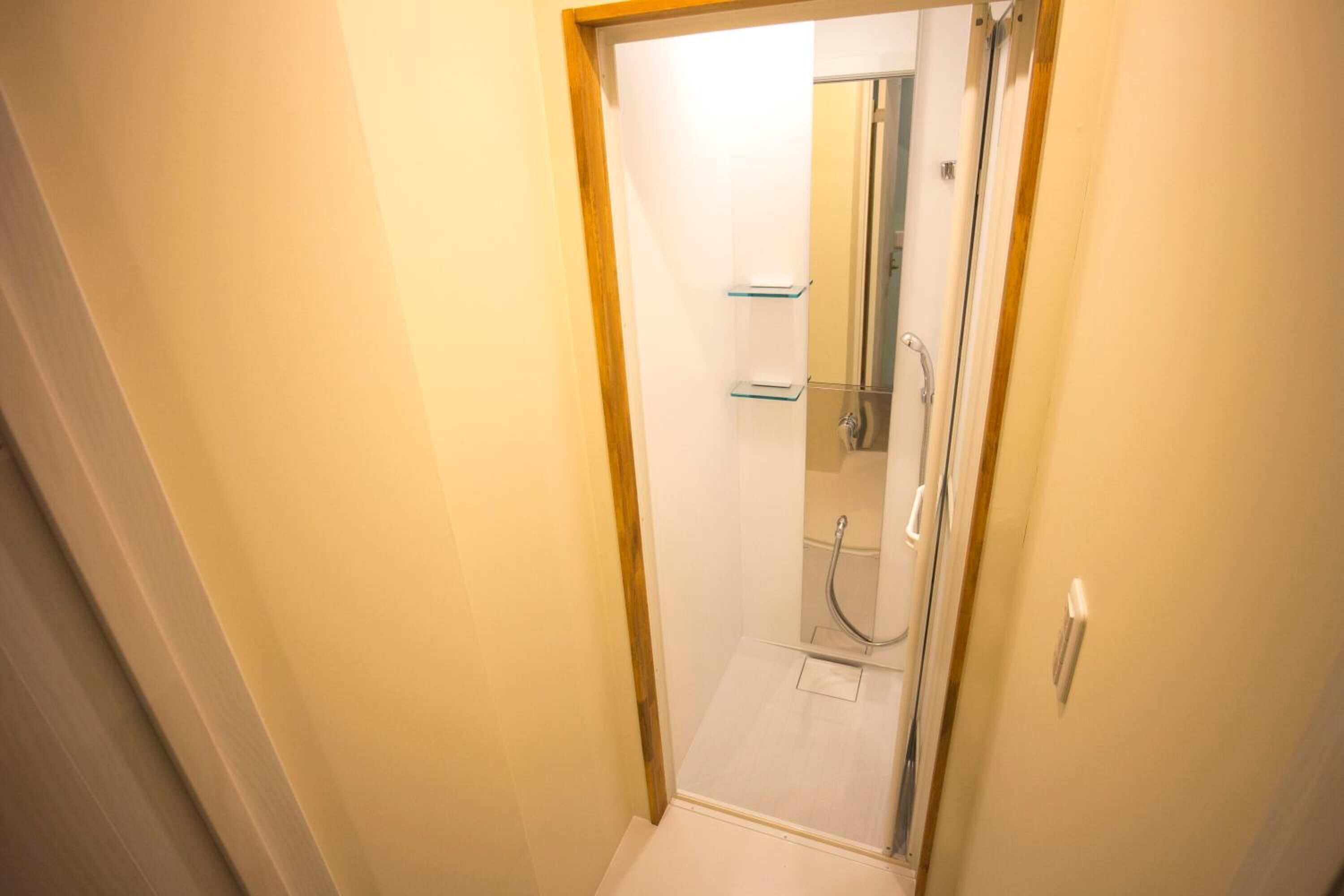 A narrow hallway leading to a glass-enclosed shower area with a visible showerhead and a small shelf.