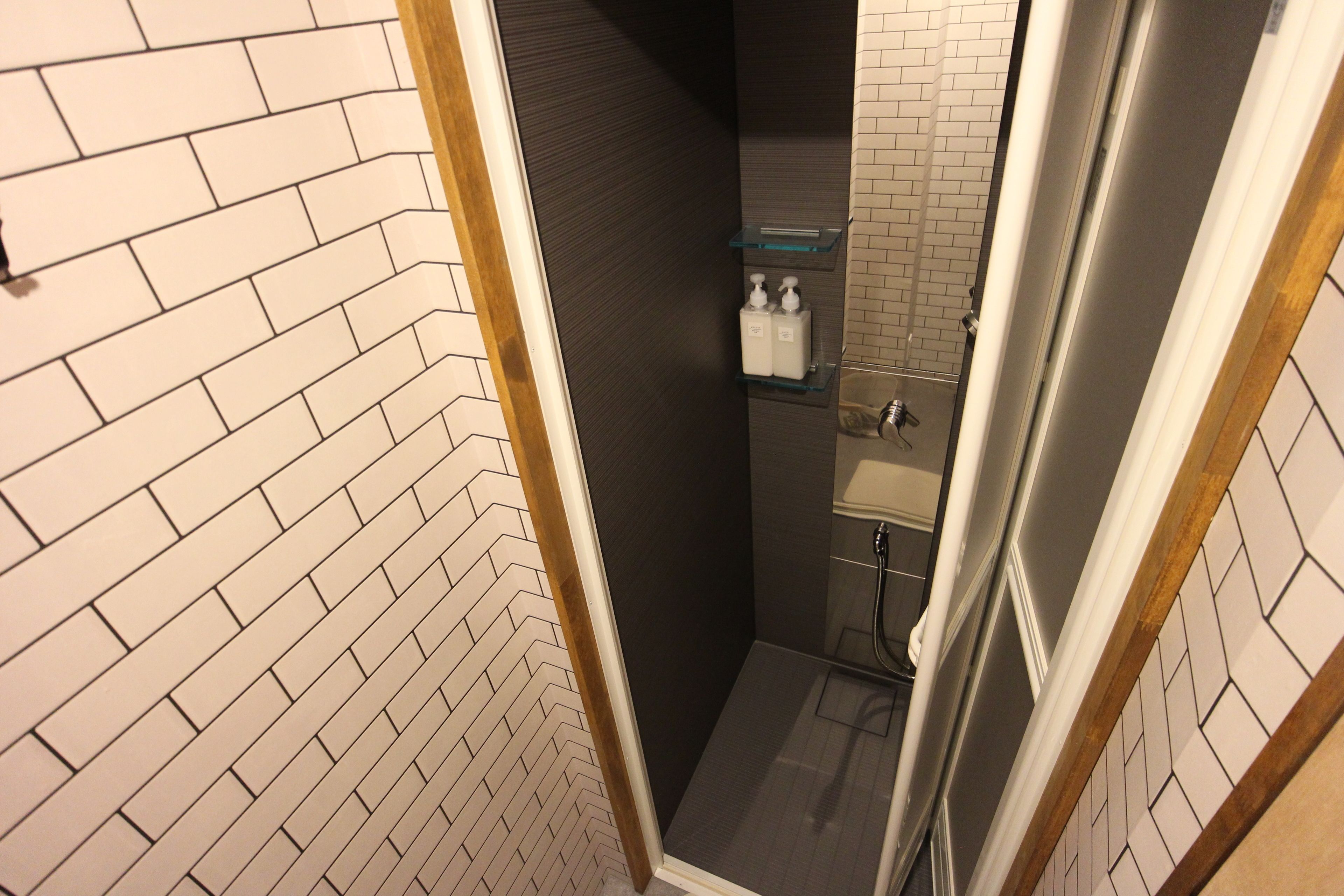 Un baño estrecho con un patrón de baldosas en espiga en las paredes, piso oscuro y estante de vidrio con artículos de aseo.