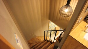 A wooden staircase with a modern pendant light, a view of a cityscape through a window, and a wooden countertop with a sink. - SHARIN Kanazawa Traveler's Inn - Hostel (Kanazawa)