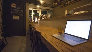 A bar area with a laptop on the counter, wooden chairs, and a menu board on the wall. - SHARIN Kanazawa Traveler's Inn - Hostel (Kanazawa)