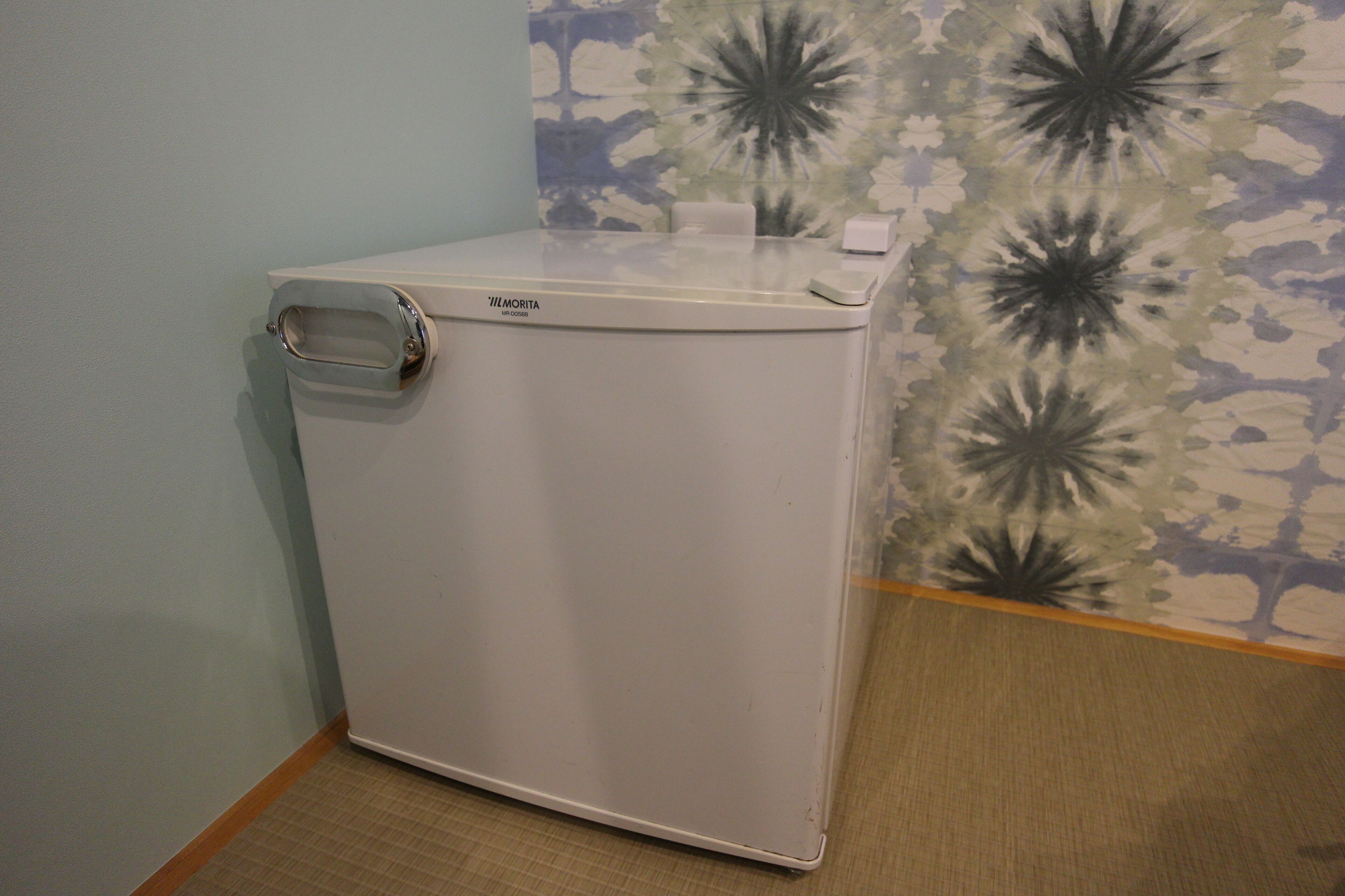 A compact, white portable washer-dryer unit with a handle on the left side, placed against a wall with a floral wallpaper pattern.
