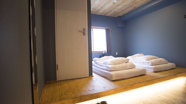 A bedroom with a wooden floor, a bed with white bedding, a window, and a door. - SHARIN Kanazawa Traveler's Inn - Hostel (Kanazawa)