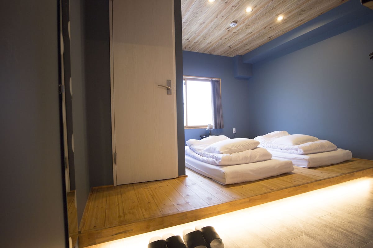 Un dormitorio con suelo de madera, una cama con ropa blanca, una ventana y una puerta.