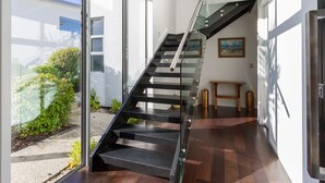 Un escalier moderne avec des rampes en verre, menant à l’étage supérieur.