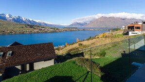 Une maison moderne dotée d’un balcon en verre donnant sur un lac et des montagnes.
