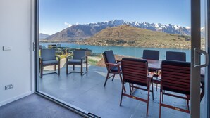 Une chambre moderne dotée d’une grande porte-fenêtre coulissante qui donne sur une terrasse extérieure offrant une vue sur les montagnes et un lac.
