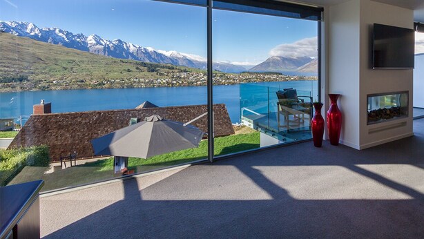 Un intérieur moderne avec une grande baie vitrée offrant une vue panoramique sur un lac et des montagnes.