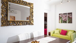 Una zona pranzo con un tavolo di legno, sedie bianche, uno specchio decorativo e un divano verde.