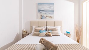 Un letto rifatto con lenzuola a righe, un cuscino raffigurante una spiaggia e un asciugamano sul letto.