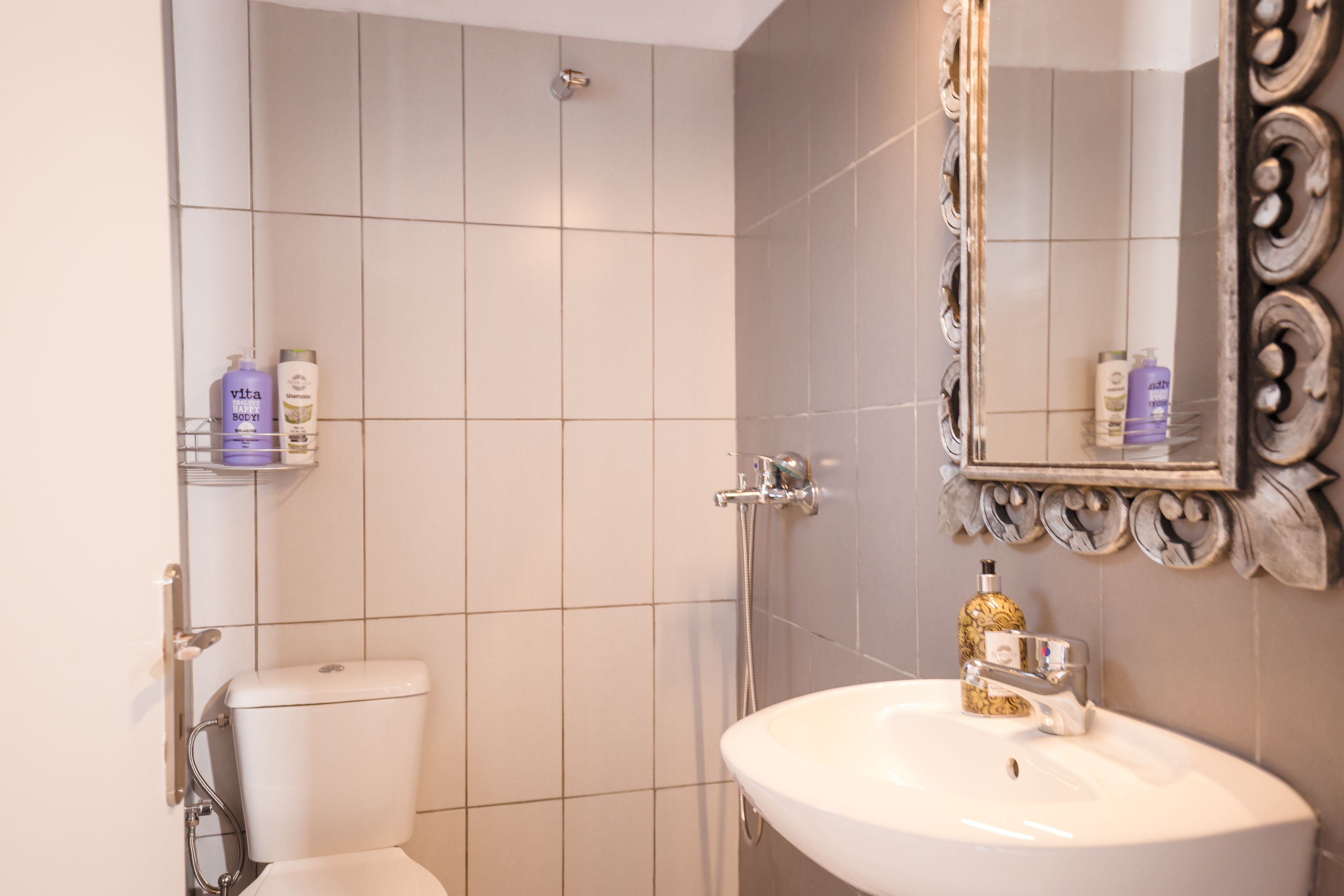 A bathroom with a white toilet, a sink, and a shower. There are toiletries on the wall.