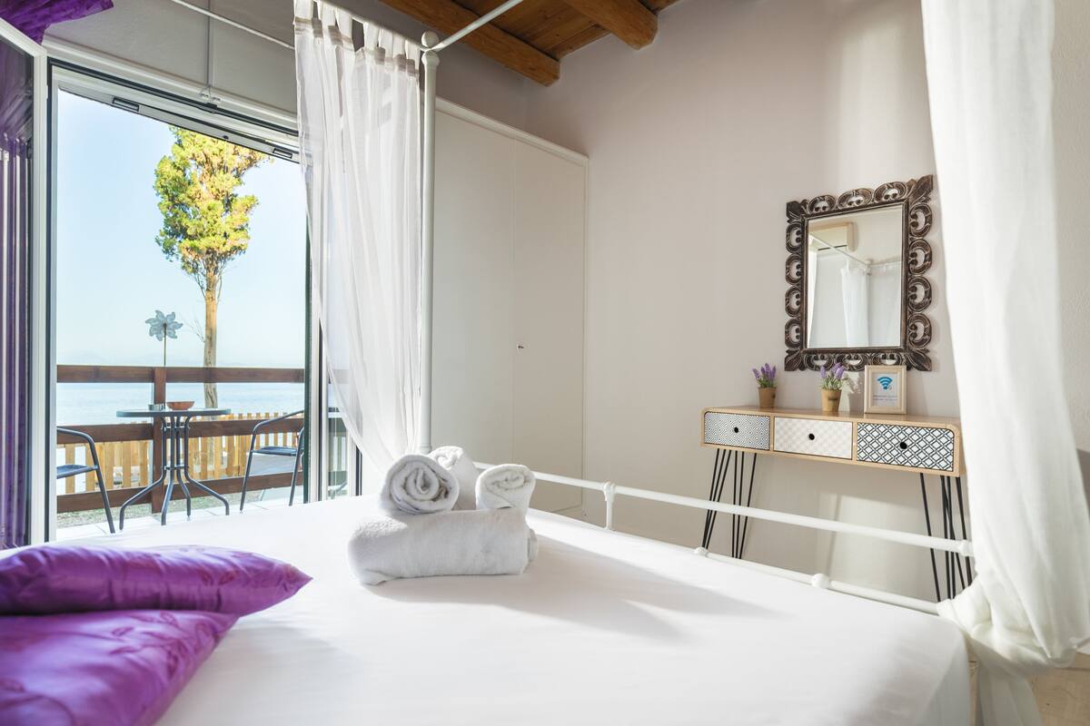 A bedroom with a bed, a bedside table with a mirror, and a view of the outdoors.