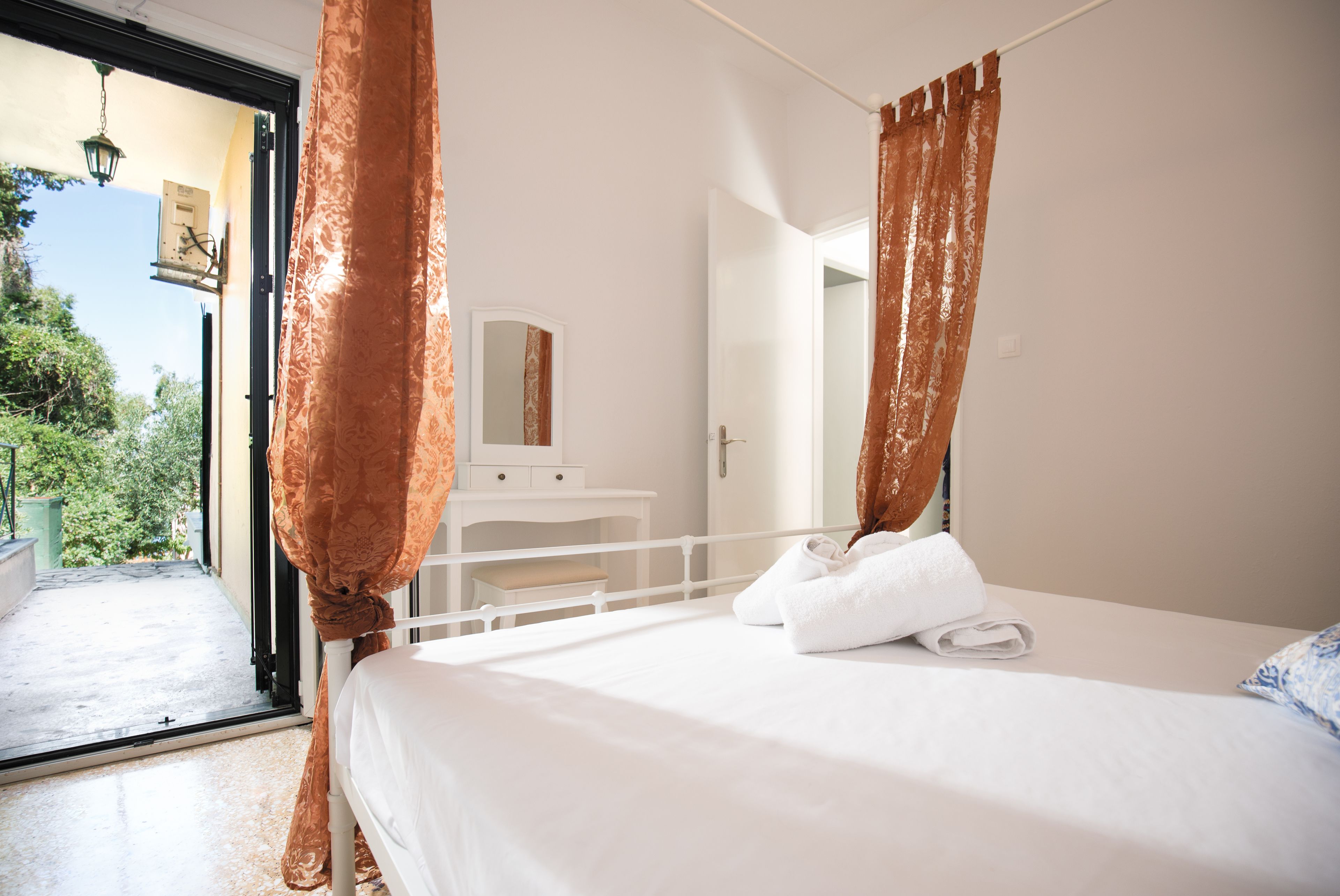 A bedroom with a bed, a nightstand, a mirror, and a view of greenery outside.