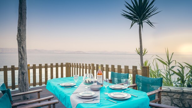 Tavolo imbandito per due con vista sul mare, un pontile in legno e un muro in pietra.