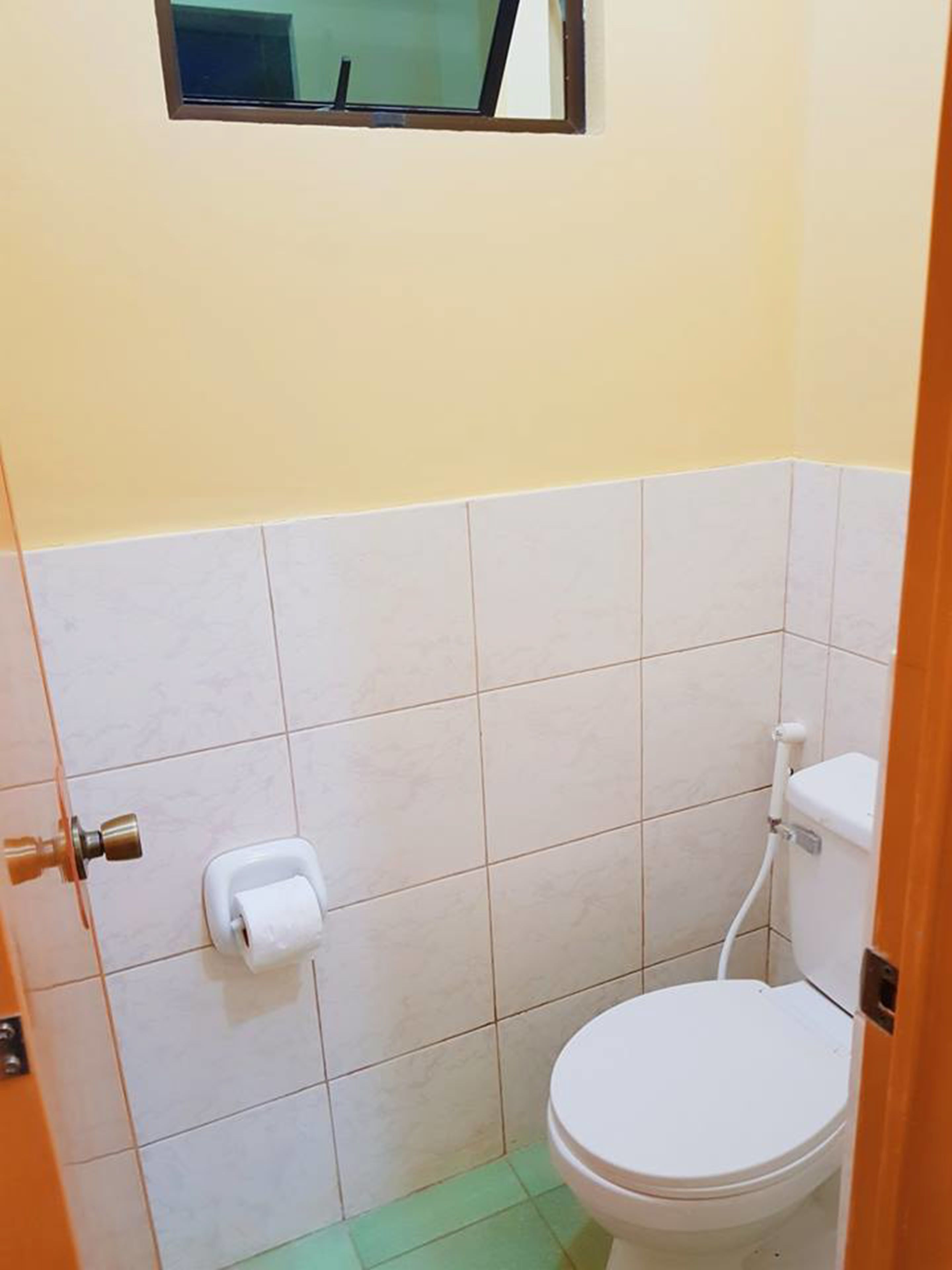 A small bathroom with a toilet, a roll of toilet paper, and a window above the toilet.