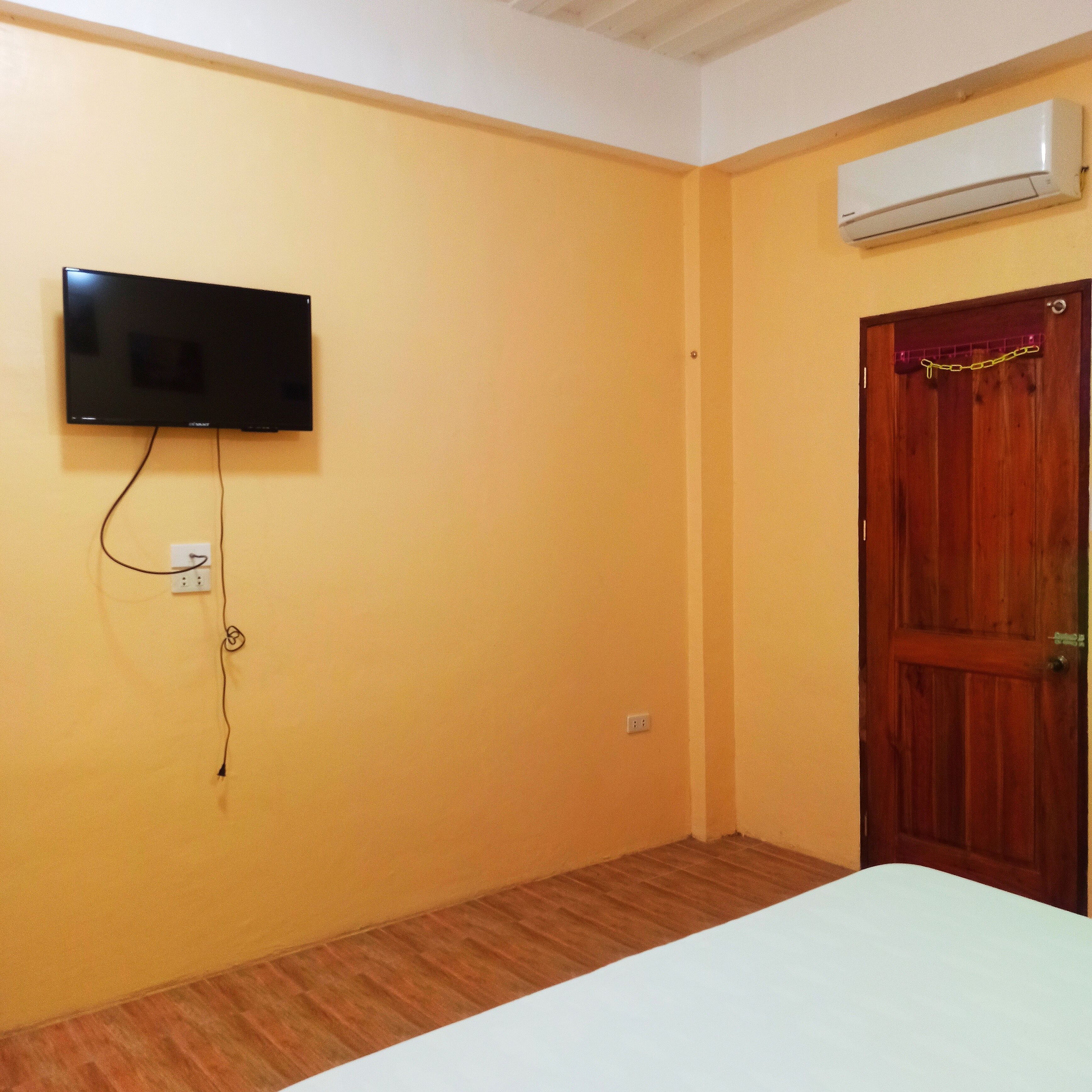 A room with a television mounted on the wall, a wooden door, and an air conditioning unit.