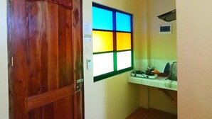 A small kitchen with a wooden door, a window with a colorful view, and a white countertop with a sink. - Pamujo Hostel (Baclayon)